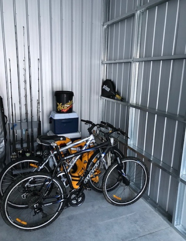 Two bikes in a storage unit, with fishing rods, tennis racket and a chilly bin in view