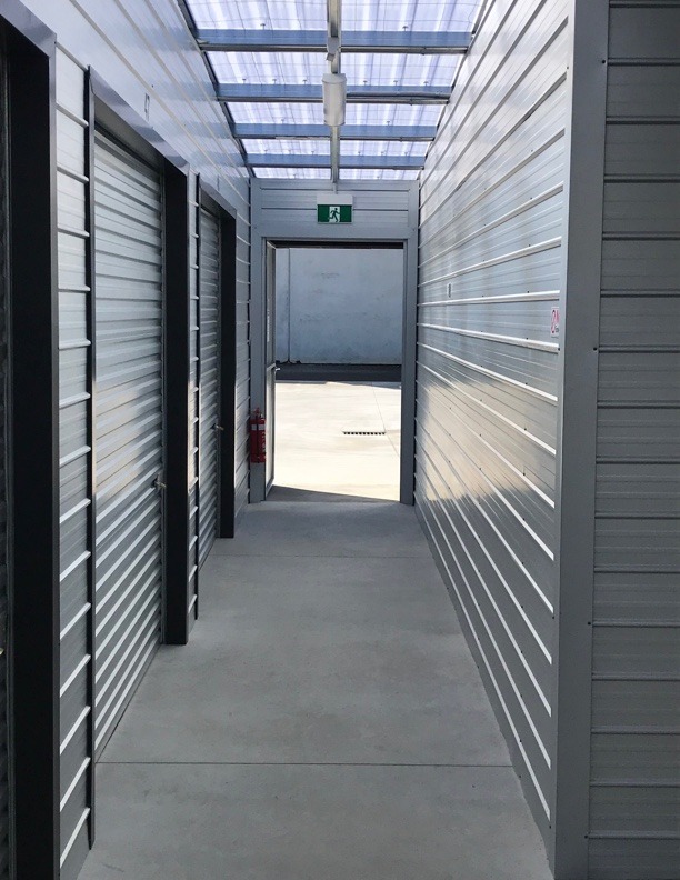 a narrow corridor, with a closed shutter on the left, leading to the outside